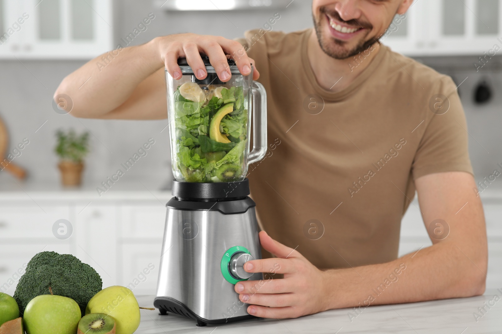 Photo of Man blending delicious smoothie at white table in kitchen, closeup