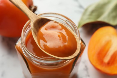 Spoon with delicious persimmon jam over jar, closeup