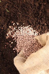 Photo of Granulated fertilizer in sack on soil, top view