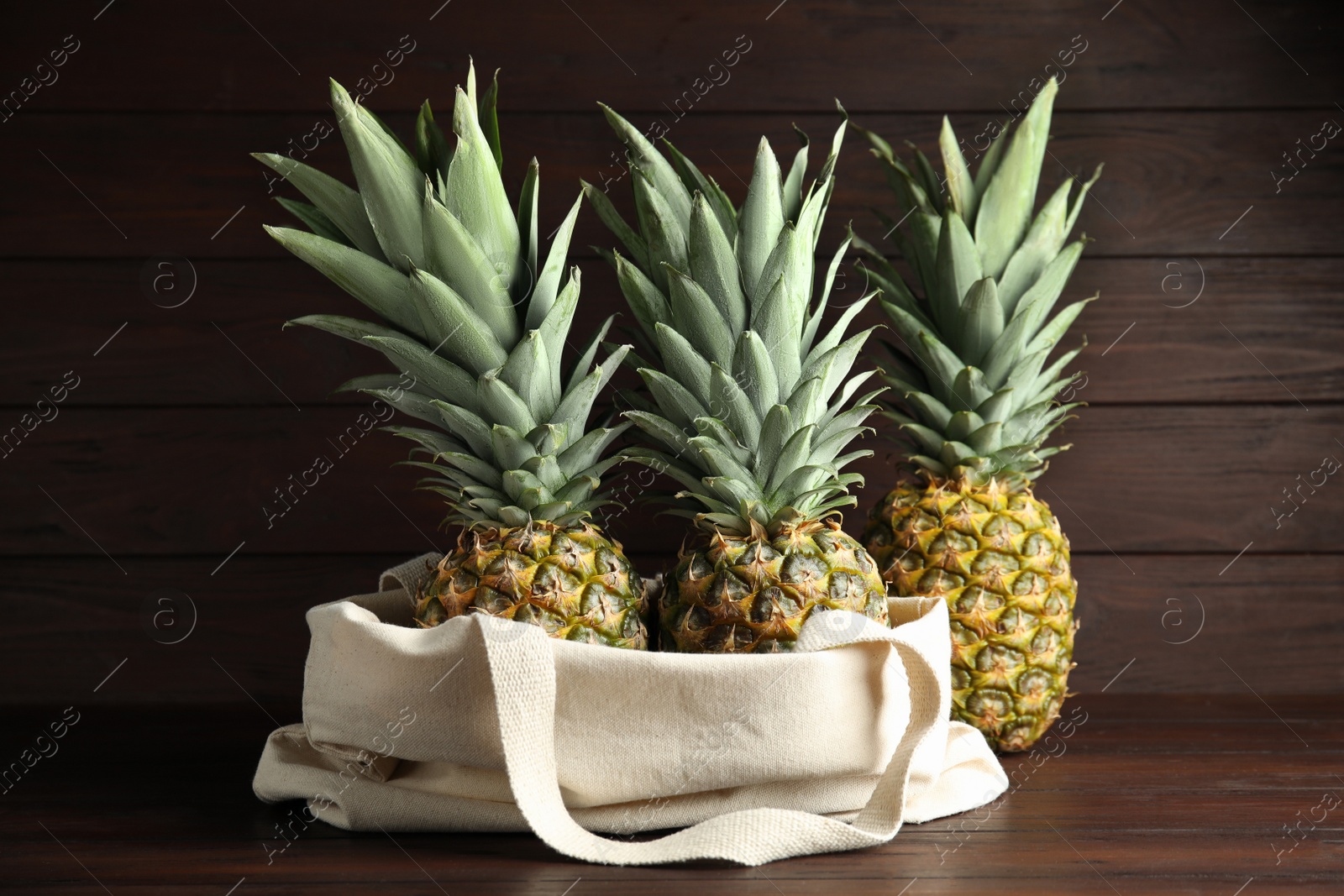 Photo of Bag with fresh juicy pineapples on wooden table