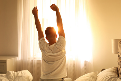 Young man stretching on bed at home, view from back. Lazy morning