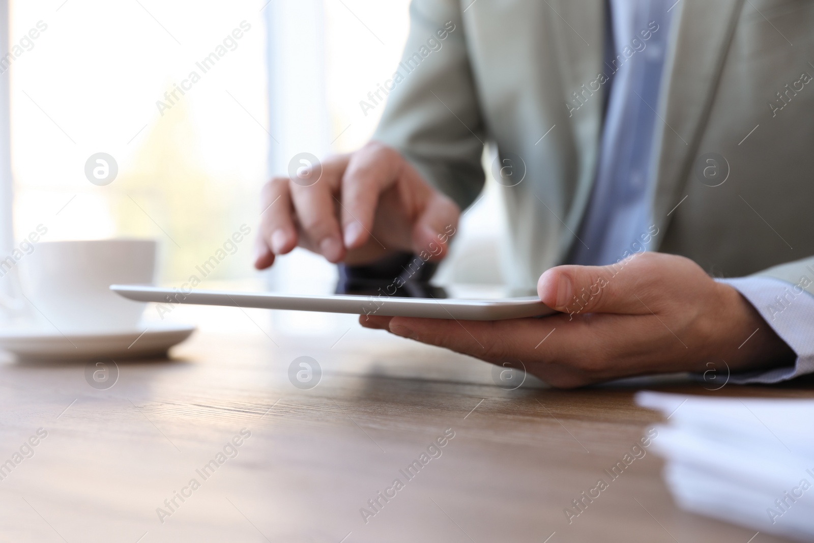Photo of Businessman working with modern tablet at wooden table in office, closeup