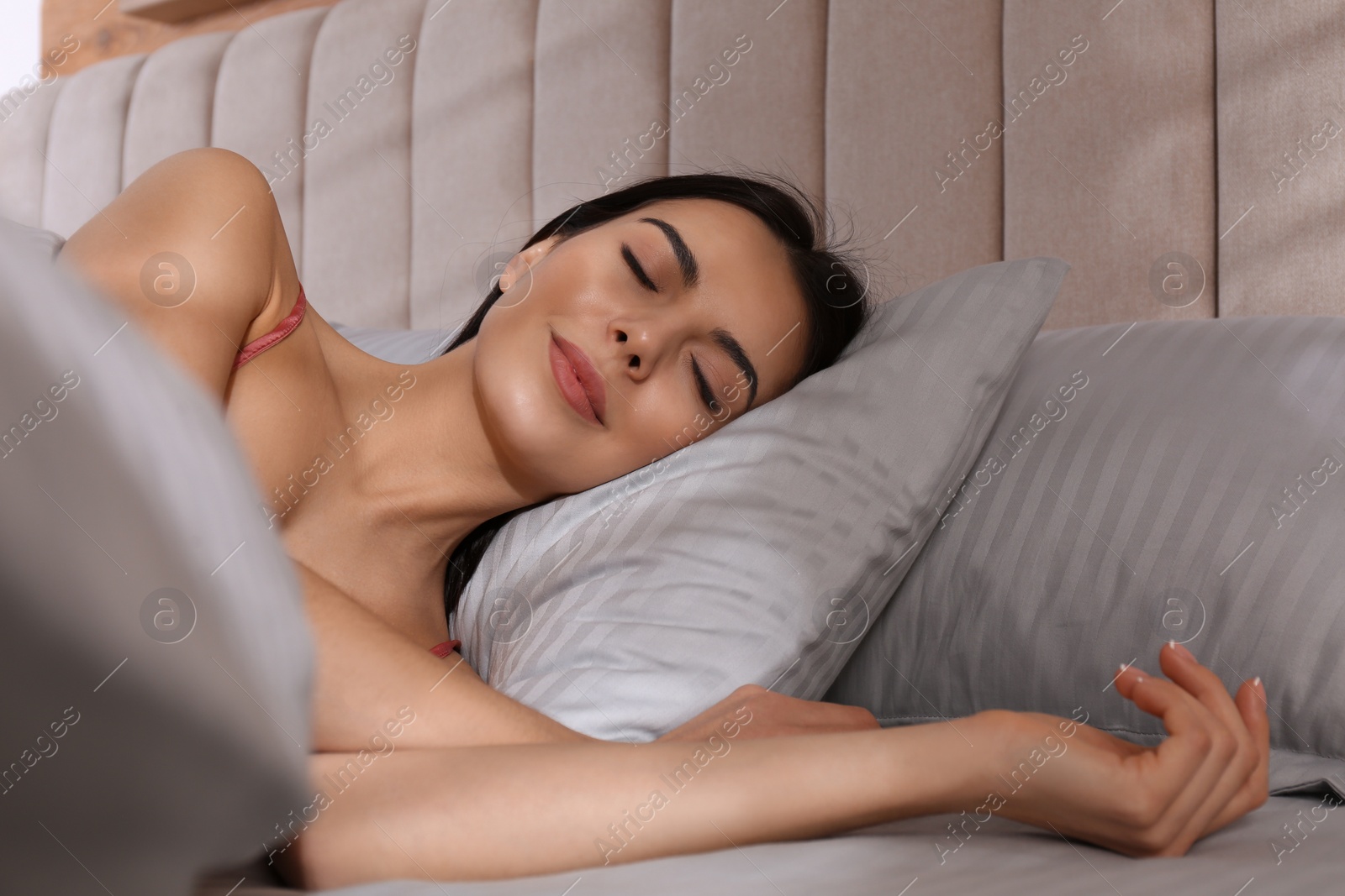 Photo of Woman sleeping in comfortable bed with light grey striped linens