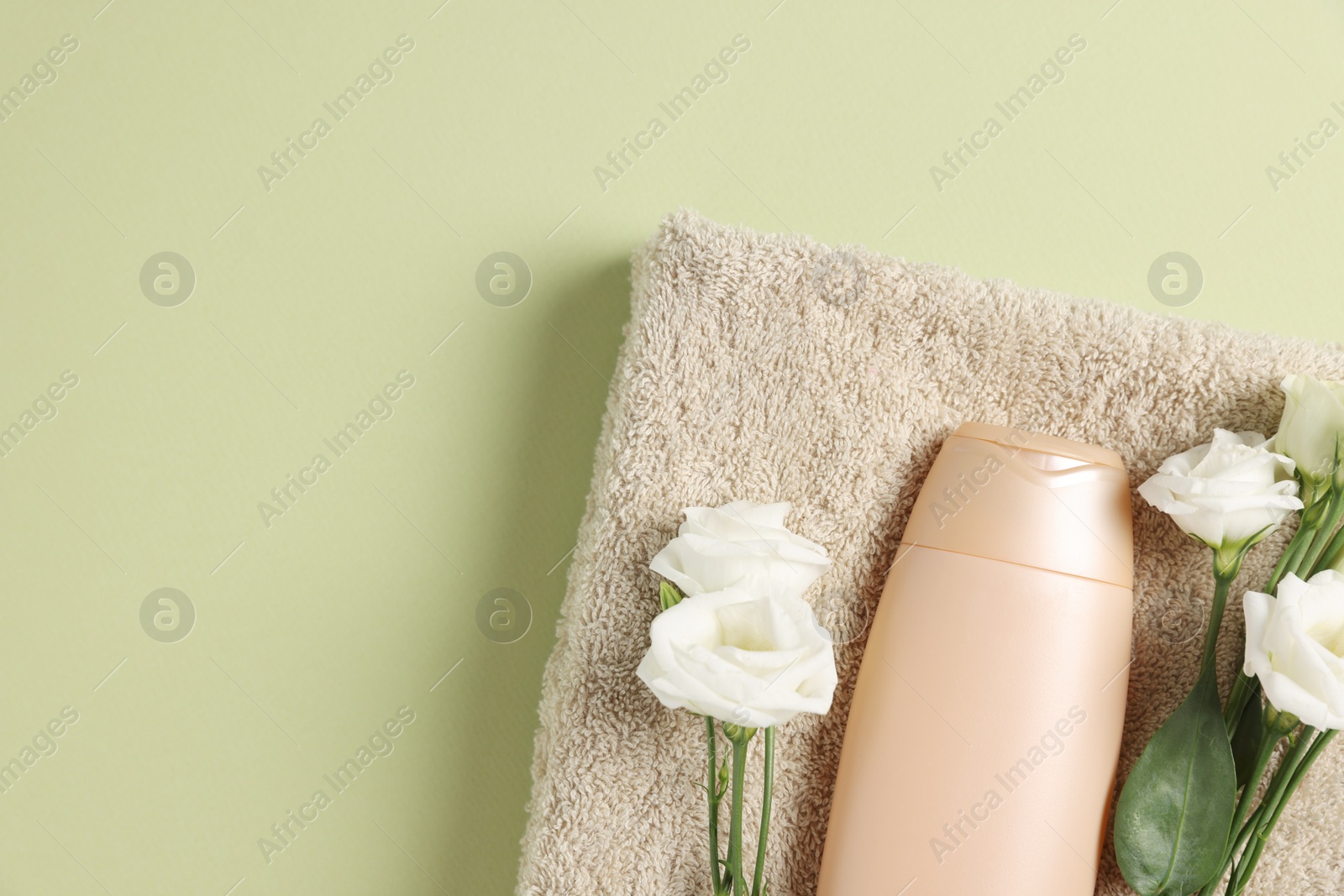 Photo of Soft folded towel with flowers and cosmetic product on green background, top view. Space for text