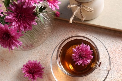 Photo of Beautiful chrysanthemum flowers and cup of tea on beige textured table, above view