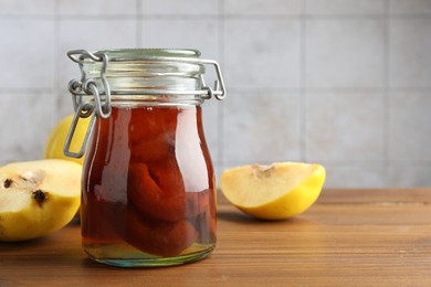 Tasty homemade quince jam in jar and fruits on wooden table, closeup. Space for text