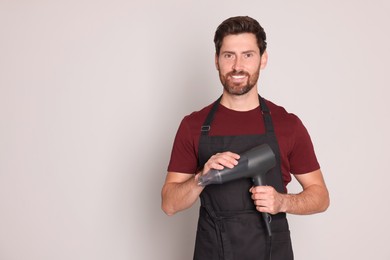 Professional hairdresser with dryer on light grey background, space for text