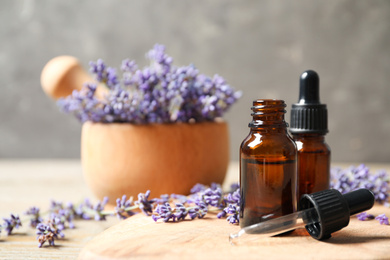 Photo of Bottles of essential oil and lavender flowers on wooden table