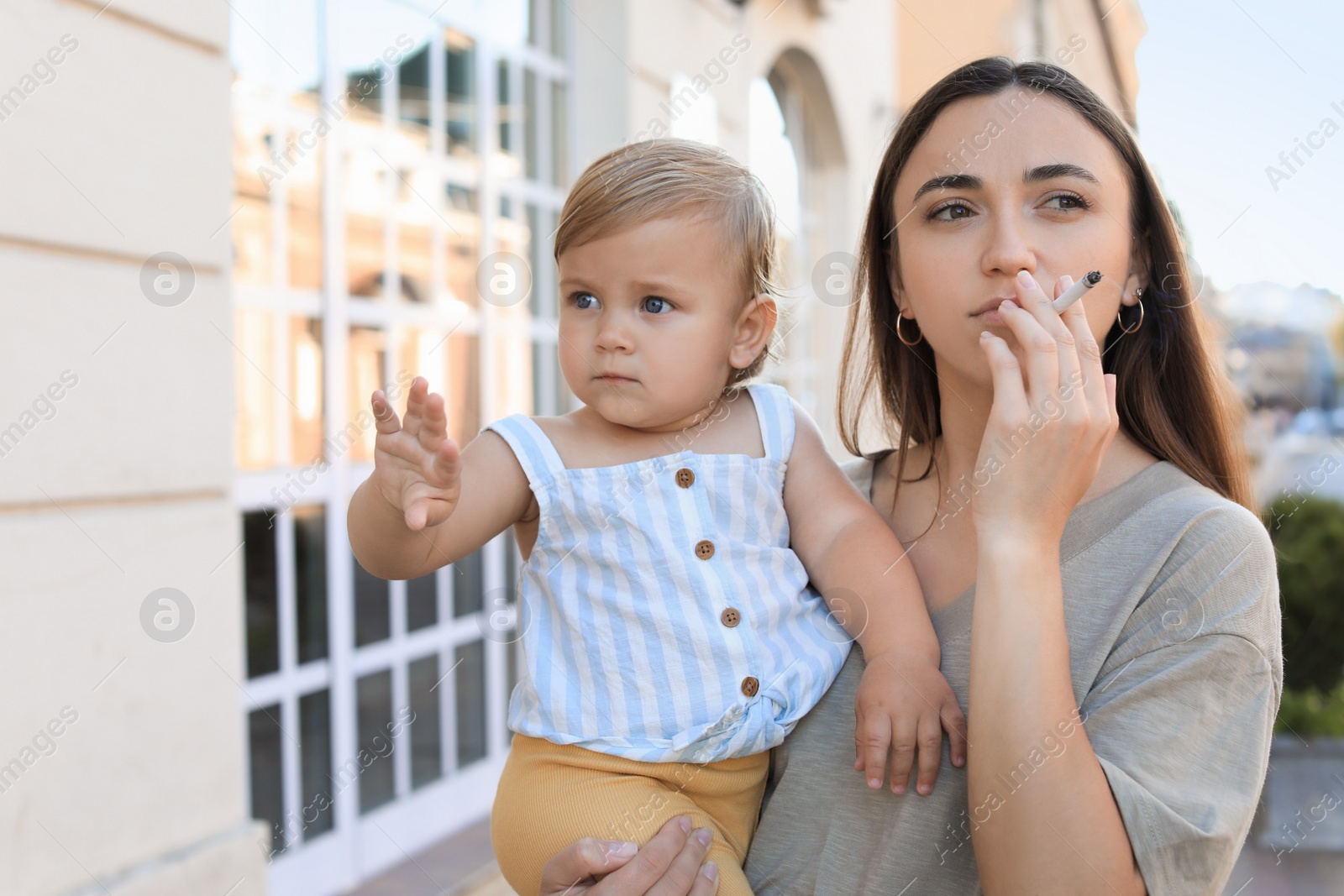 Photo of Mother with cigarette and child outdoors. Don't smoke near kids