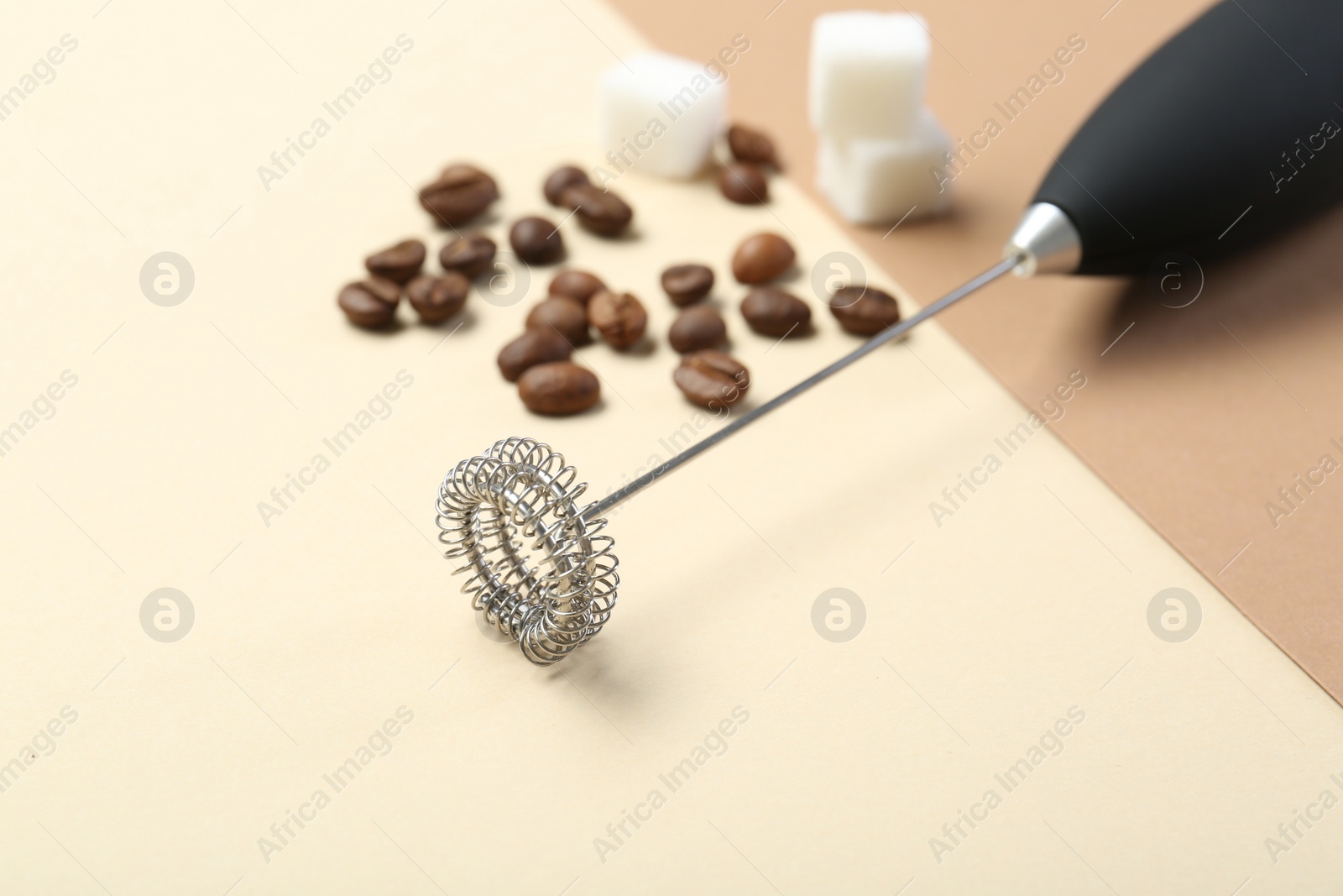 Photo of Milk frother wand, coffee beans and sugar cubes on color background, closeup