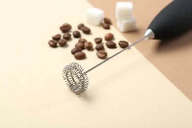 Milk frother wand, coffee beans and sugar cubes on color background, closeup