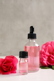 Photo of Fresh flowers and bottles of rose essential oil on table, space for text