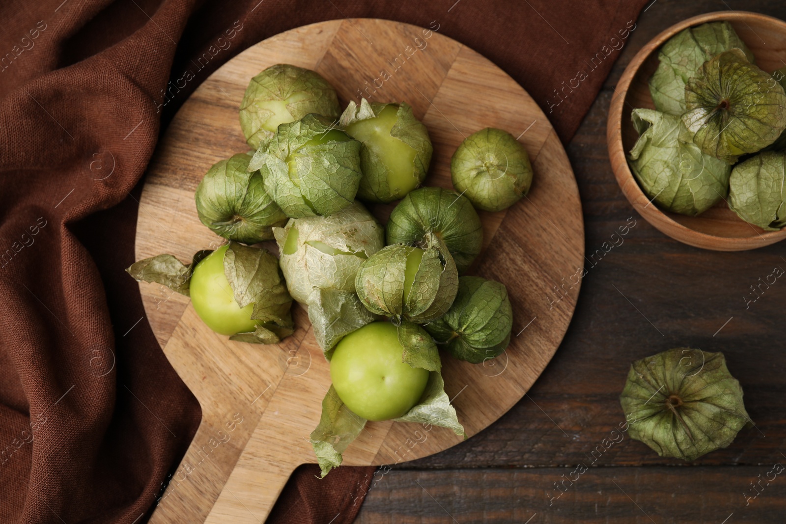 Photo of Fresh green tomatillos with husk on wooden table, flat lay