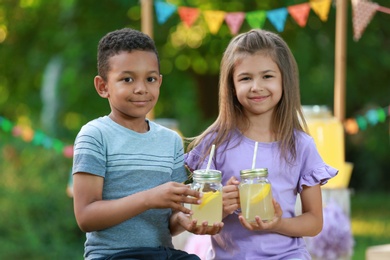 Photo of Cute little children with natural lemonade in park. Summer refreshing drink