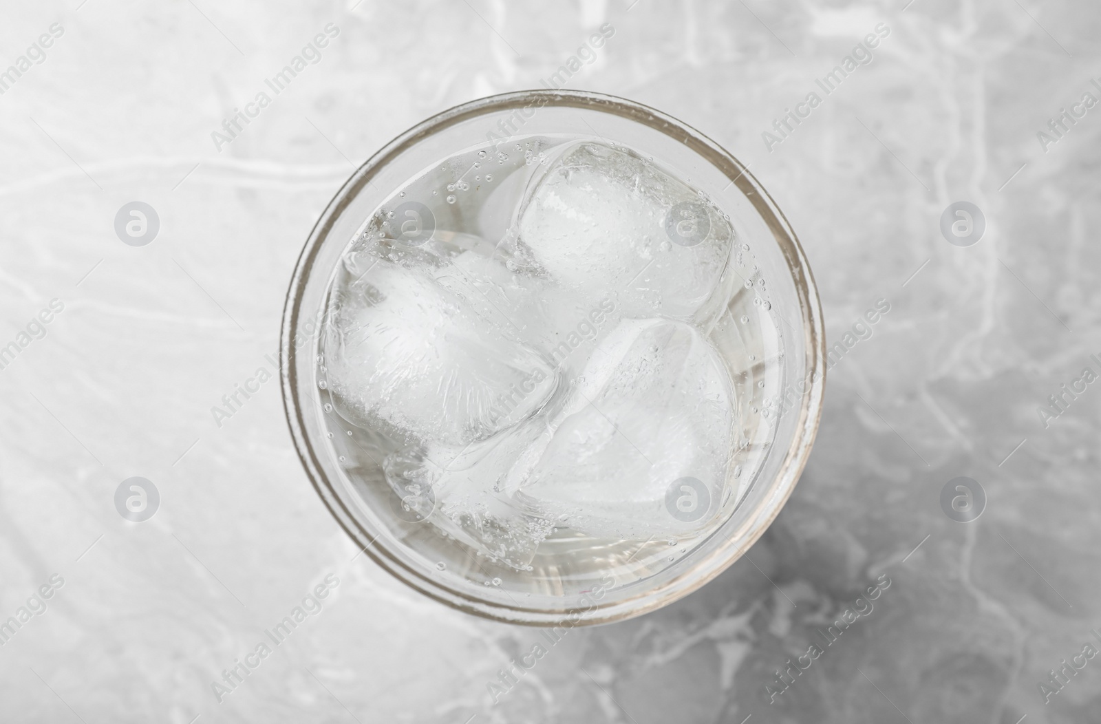 Photo of Glass of soda water with ice on grey table, top view