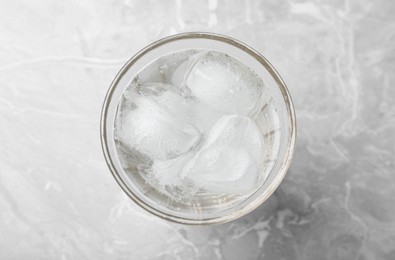 Photo of Glass of soda water with ice on grey table, top view