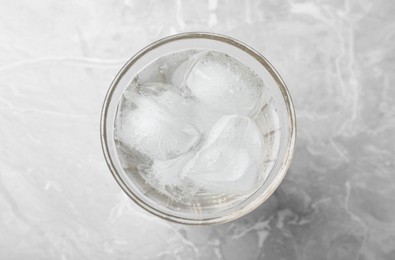 Glass of soda water with ice on grey table, top view