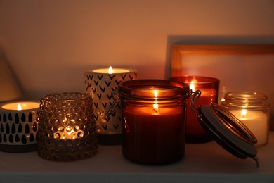 Beautiful burning wax candles on white shelf