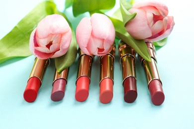 Photo of Bright lipsticks and spring flowers on light blue background