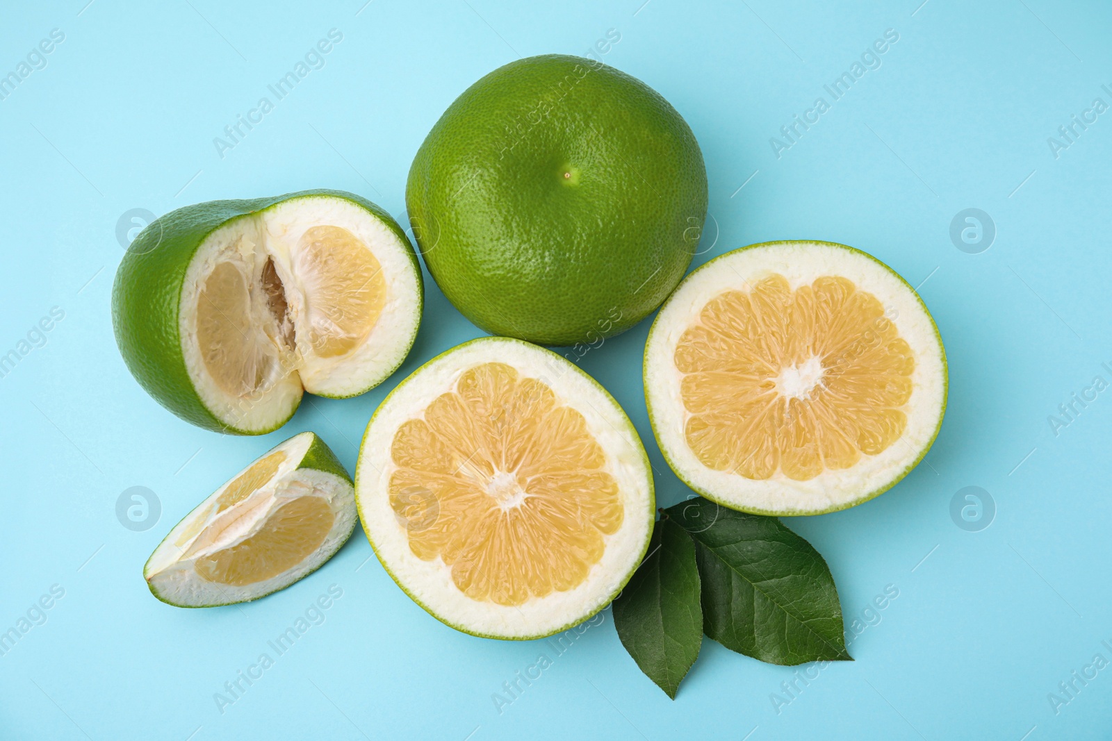 Photo of Whole and cut sweetie fruits with green leaves on light blue background, flat lay