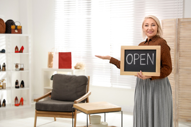 Photo of Female business owner holding OPEN sign in boutique. Space for text