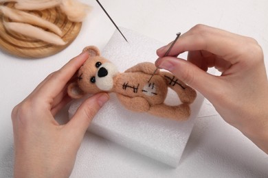 Photo of Woman felting toy bear from wool at white table, closeup