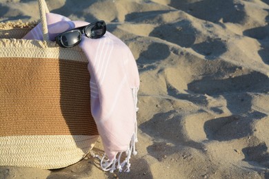 Photo of Stylish wicker beach bag, sunglasses and blanket on sand. Space for text