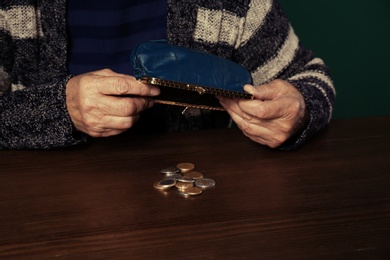 Photo of Poor senior woman with empty wallet and coins at table, closeup