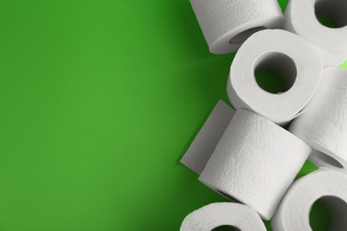 Photo of Soft toilet paper rolls on green background, flat lay. Space for text