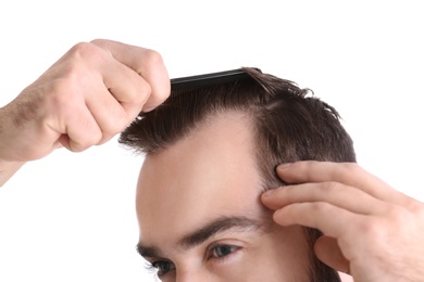 Photo of Young man with comb on white background, closeup. Hair loss problem