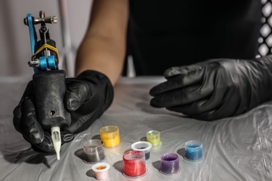 Photo of Tattoo artist with machine and inks at table, closeup