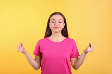 Photo of Young woman meditating on yellow background. Stress relief exercise