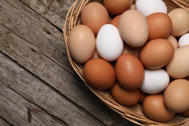 Photo of Fresh chicken eggs in wicker basket on wooden table, top view. Space for text