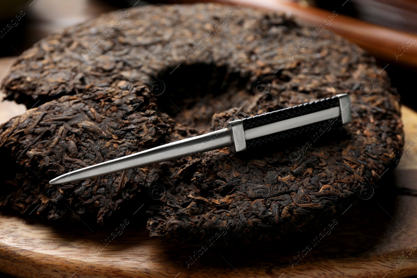 Photo of Broken disc shaped pu-erh tea and knife on wooden board, closeup