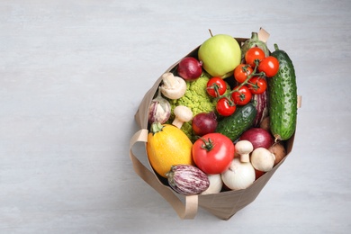 Paper bag full of fresh vegetables on light background, top view. Space for text