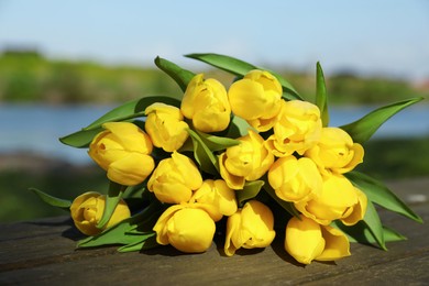 Photo of Bouquet of beautiful yellow tulips on wooden table outdoors, closeup