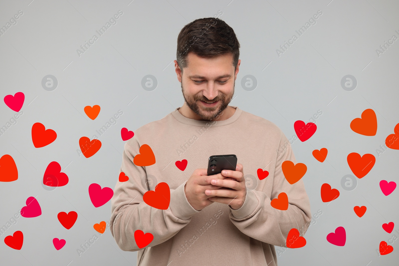 Image of Long distance love. Man chatting with sweetheart via smartphone on grey background. Hearts flying out of device and swirling around him