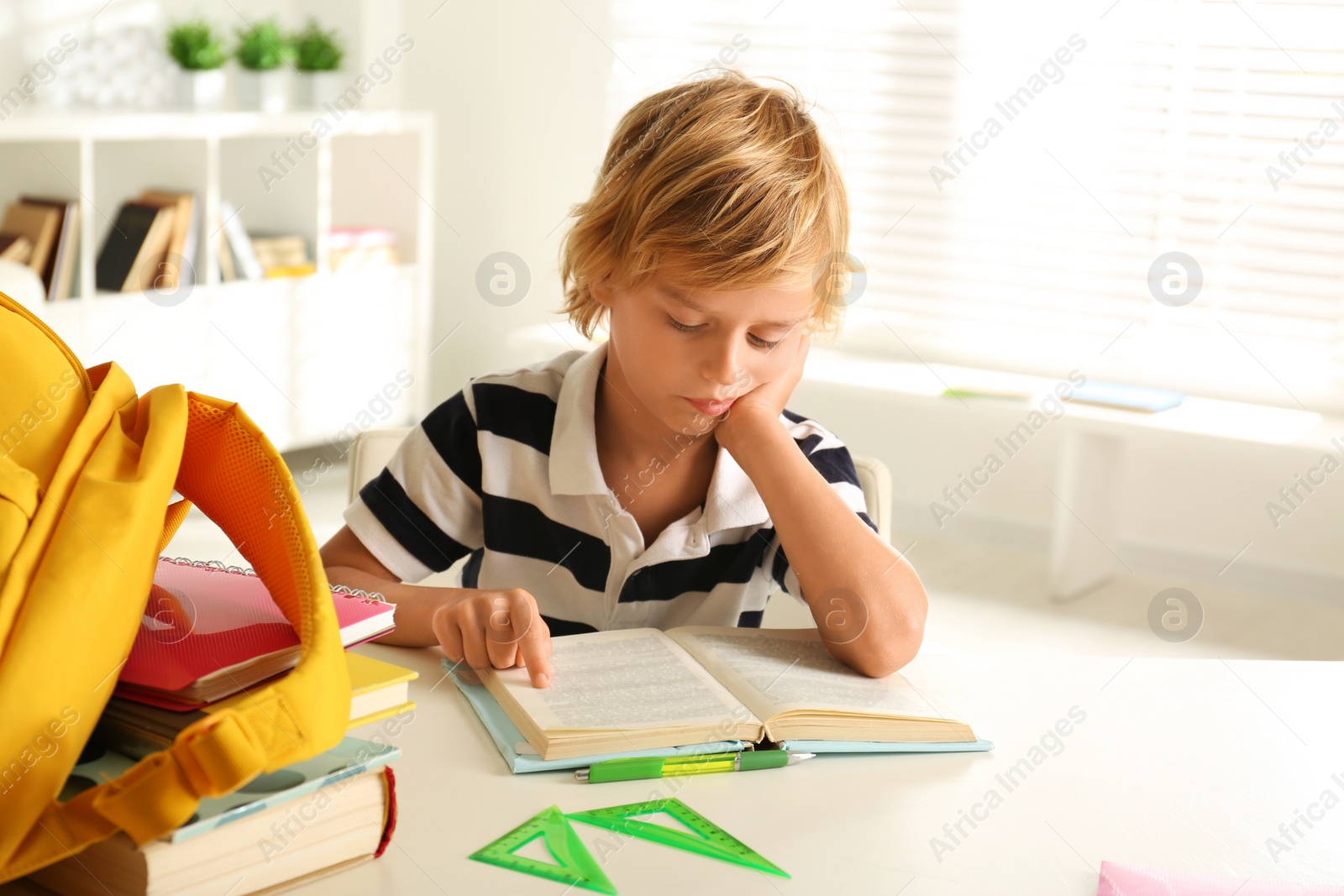 Photo of Bored little boy doing homework at table indoors