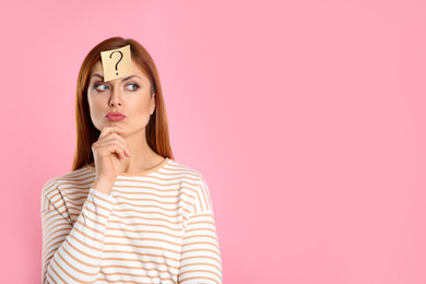 Photo of Pensive woman with question mark sticker on forehead against pink background. Space for text