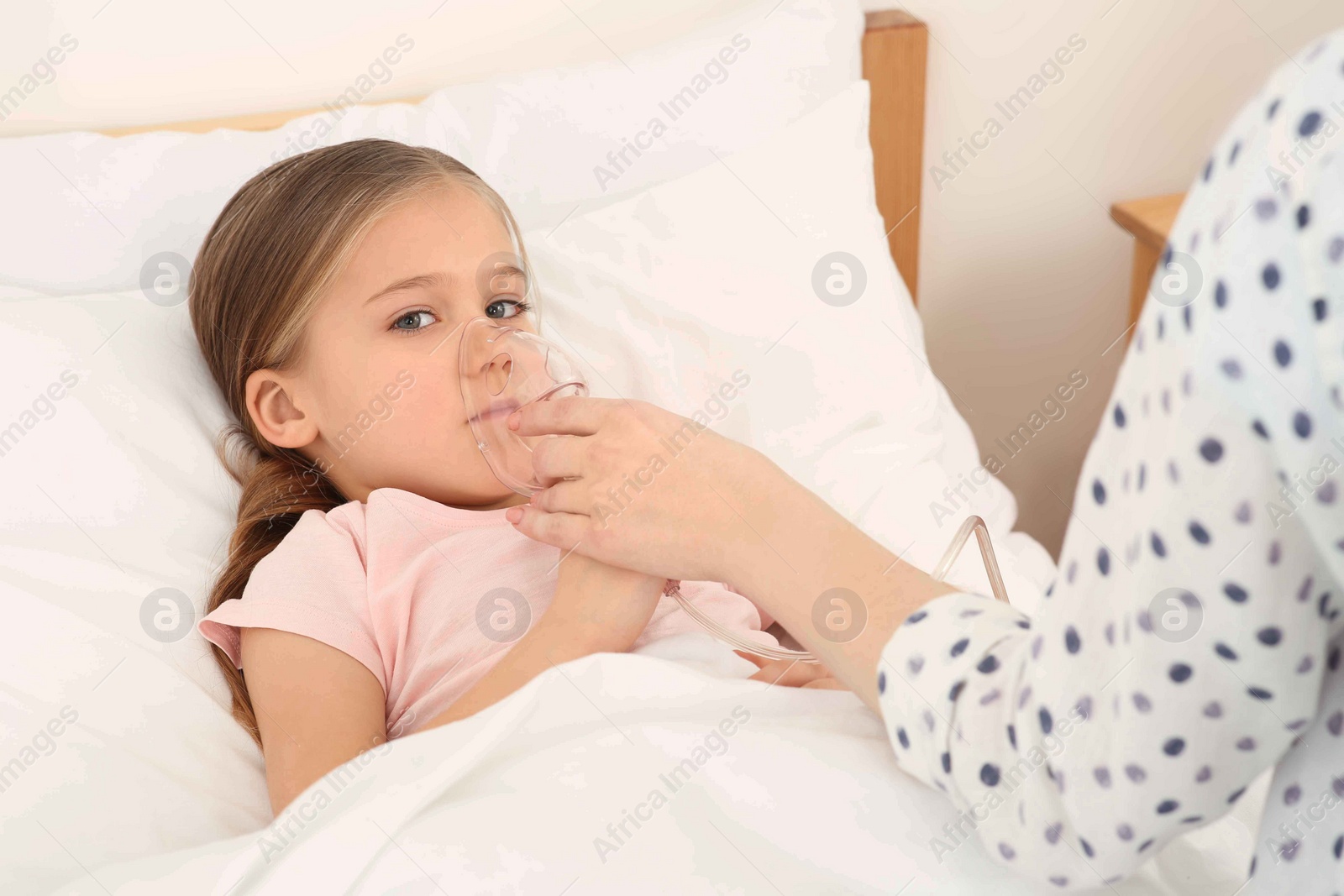 Photo of Mother helping her sick daughter with nebulizer inhalation in bedroom