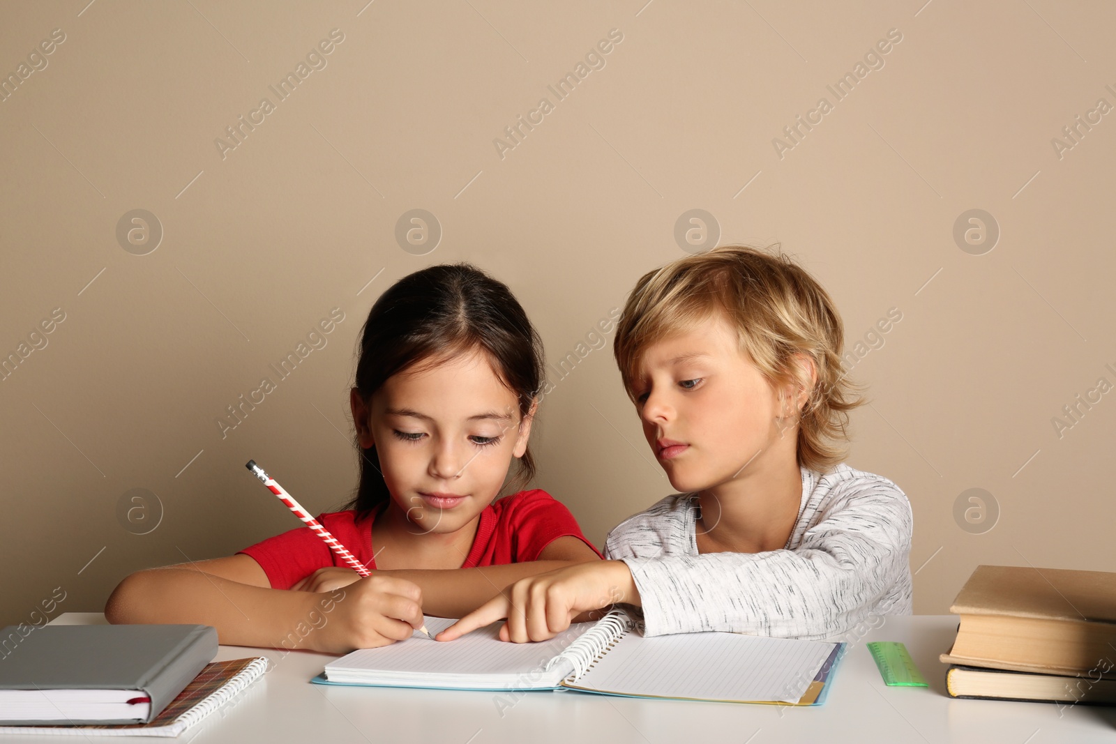 Photo of Little boy and girl doing homework at table on beige background