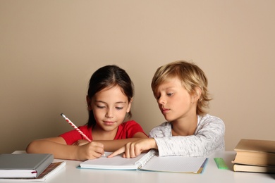 Little boy and girl doing homework at table on beige background