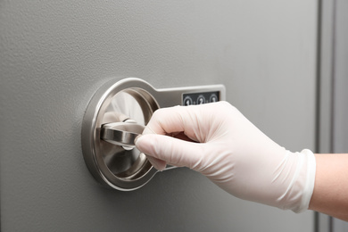 Photo of Woman in gloves opening modern safe, closeup