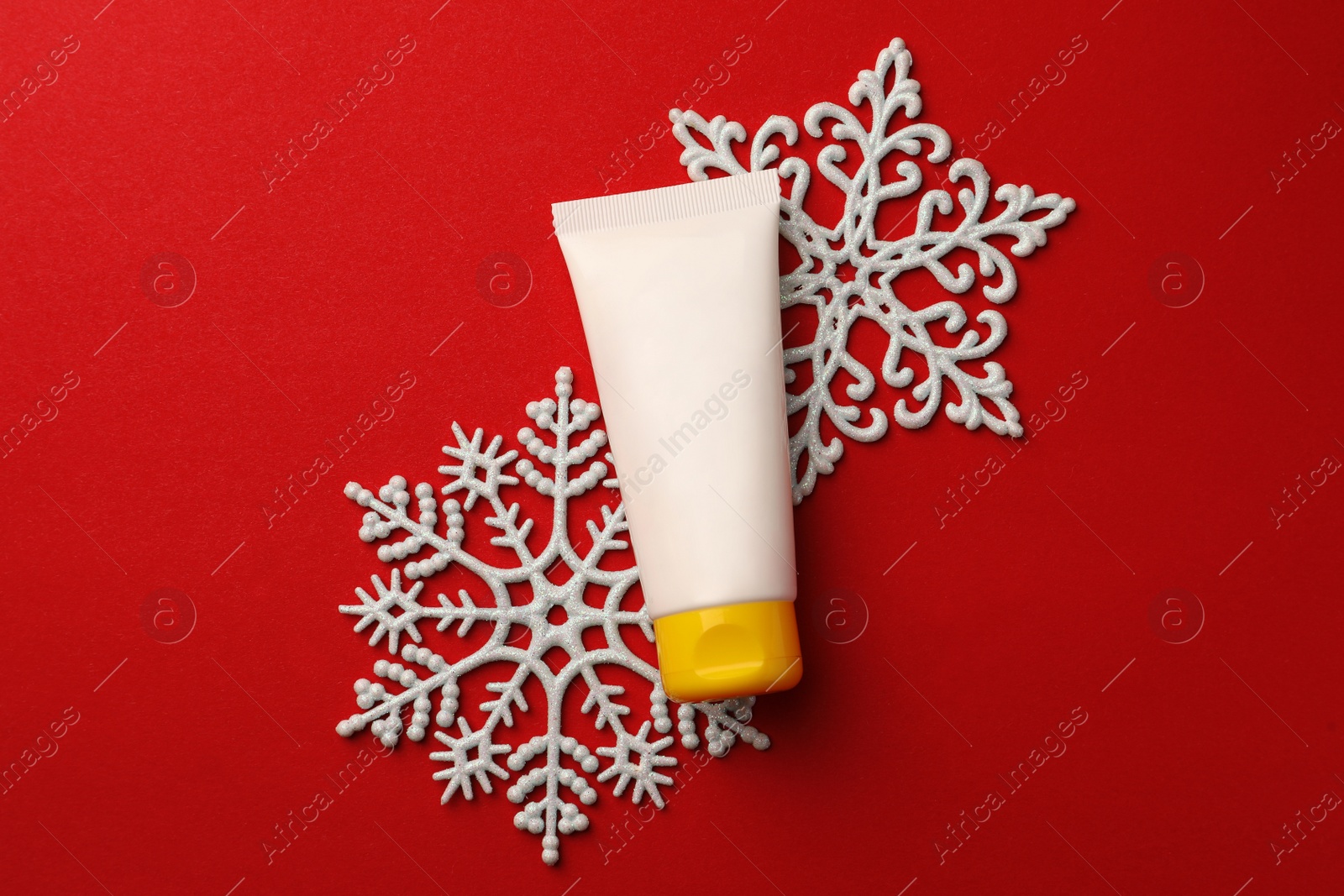 Photo of Tube of hand cream and snowflakes on red background, flat lay. Winter skin care