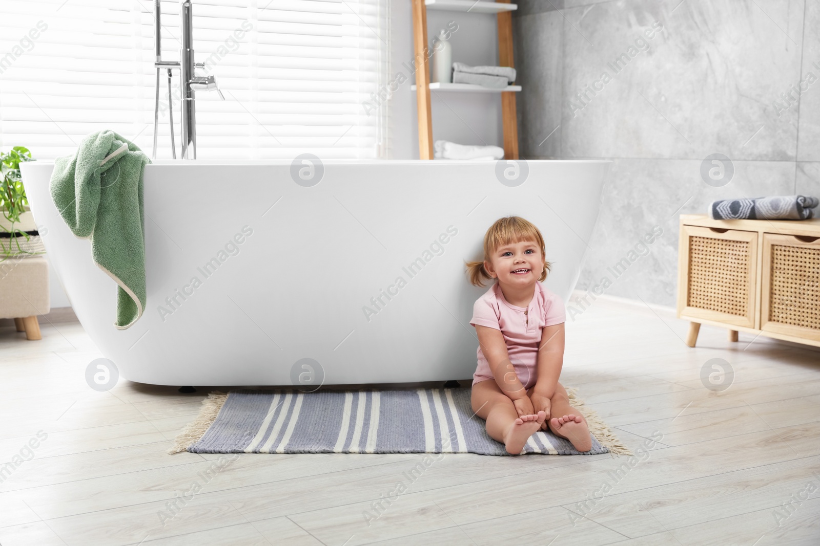 Photo of Cute little girl near tub in bathroom