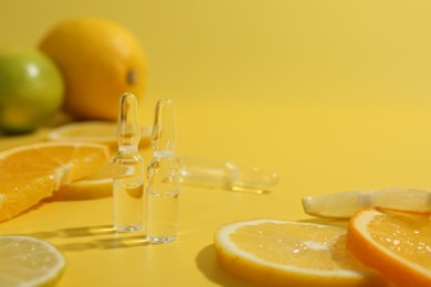 Photo of Skincare ampoules with vitamin C and citrus slices on yellow background, closeup. Space for text