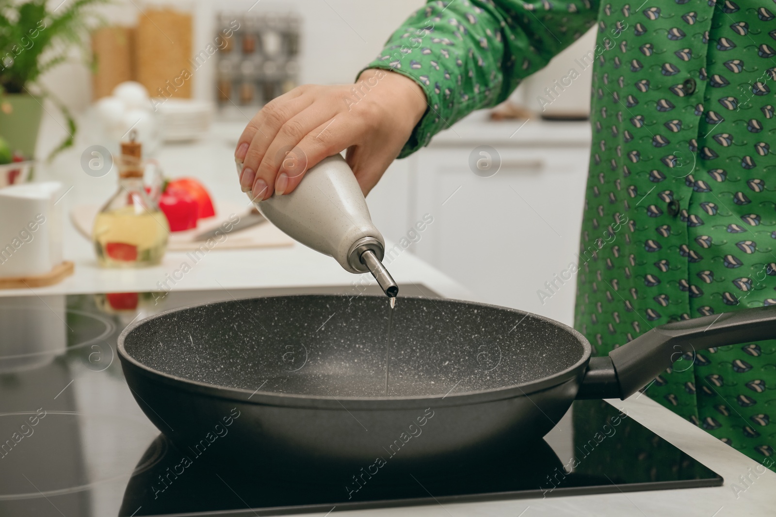 Photo of Woman pouring oil from bottle into pan in kitchen, closeup