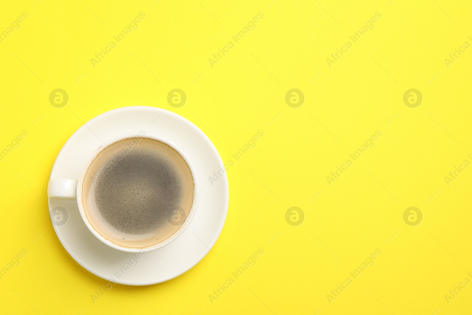 Photo of Aromatic coffee in cup on yellow background, top view. Space for text