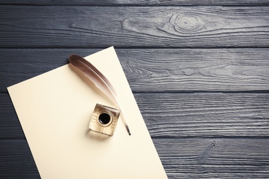 Photo of Feather pen, inkwell and blank parchment on wooden table, top view. Space for text