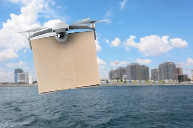 Image of Modern drone with carton box flying above sea on sunny day. Delivery service 